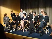 The cast seated in director's chairs