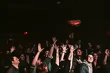 A crowd reaches for a frisbee that is being thrown from a stage.