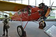 Small airplane with single wing over top; single wooden propeller in front; "Newsboy" painted on fuselage