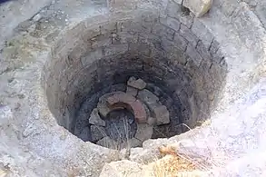Hole in the floor supported by circular bricks. At the bottom of the hole several bricks are stored.