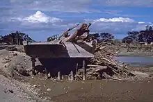 Image showing a mangled bridge split across a river with wood debris piled up against a section of the bridge.