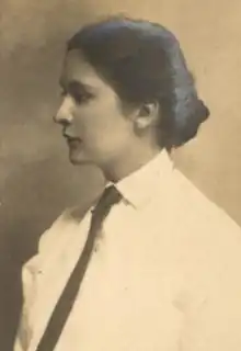 A young white woman with dark hair dressed to the nape, wearing a collared white shirt and a dark necktie