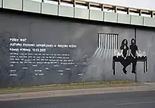 A stark black, white, and gray mural depicting two members of the group sitting on a bench with prison bars in the background.