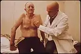 A bald physician listens with a stethoscope to the chest of an old, bare-chested man