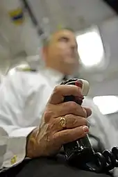 Photograph of a hand holding a pistol grip; the grip has a red trigger button and a coiled cable connected to its base.
