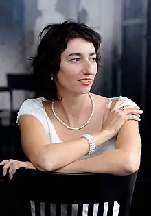dark-haired white female sitting backwards on a chair, looking left of camera and smiling