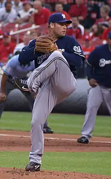 A man wearing a navy blue Brewers jersey, gray pants, and a navy blue cap shown preparing to throw a ball from the pitcher's mound