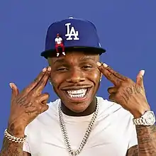 Cover art depicting DaBaby smiling and pointing finger guns at his head.  He wears a baseball hat and a smaller version of himself is sitting on the brim.