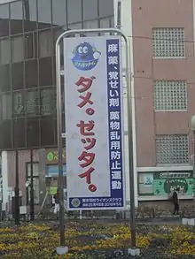 A roadside sign with a cartoon globe above a Japanese slogan in large bold text