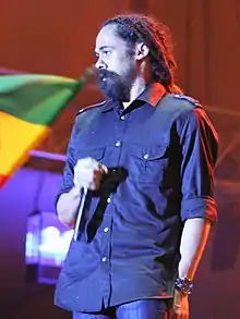 A man holding a microphone on a stage and wearing a blue shirt.