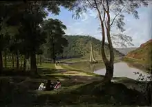 Four people sit together on a shaded lawn beside a riverside path. A small boat sails on the river, which bends away into a gap between sunlit wooded hills.