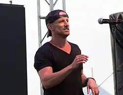Singer Daniel Powter standing at a microphone while wearing a dark baseball cap