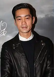 Danny Chan wearing a white shirt, dark sweater, and black leather jacket, smiling at camera