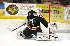 Hockey goaltender kneels on the ice and reach to his left with his glove