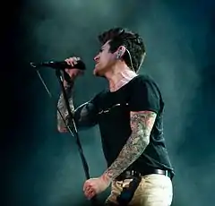 A color photograph of American musician Davey Havok performing live in 2009, dressed in a black shirt and holding a microphone stand.