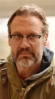 David Matásek with short hair and facial hair, wearing brown jacket and glasses, looking left of camera