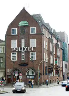 A 3 floor red-brick building, with the German word 'police' in large letters between first and second floor. The windows are white sash windows.