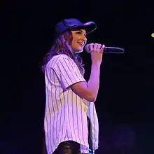 A woman wearing a cap and smiling while holding a microphone in her hand