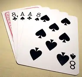A 5-card stud poker hand lays on a table showing black aces and eights, with the hole-card face down