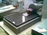 Gravestone in black marble, with small floral tribute on it
