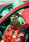 Derek Warwick in a racing suit sitting in a touring car being spoken to a team member