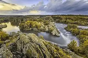 The same photograph with its colors modified to simulate red–green color blindness. The orange areas of rocks, yellowish pink areas of the sky, and green plants now appear to have similar yellowish color, while purple parts of the sky and river look blue or gray.