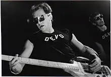 Gerald Casale performing with the rock band Devo in 1978. He is playing a Gibson Ripper bass that is meant for right-handed players, but is playing it upside down, as he is left-handed