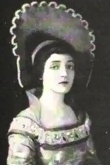 A young white woman with dark hair, wearing a costume with a very high scalloped collar that reaches above her head, and a medieval-style gown
