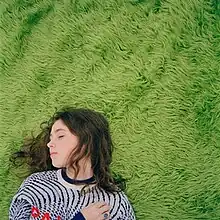 A young brunette woman laying on a green rug.