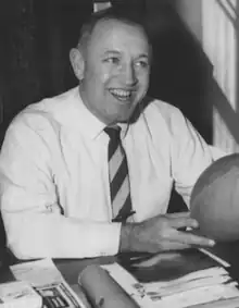 Richard F. Gallagher sitting at a table with a football in his hands in 1959