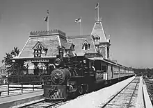 A black-and-white image of a train parked in front of a railroad station with the logo of the Atchison, Topeka and Santa Fe Railway visible on its roof