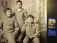 photograph of three American Indian children dressed in suits, with an inset photo in their native attire