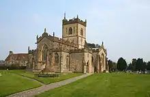 Yellow stone building with central square tower, Foregound is paths through green grass.