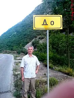 Puzzle creator Slavko Bovan next to the board with the name of village Do