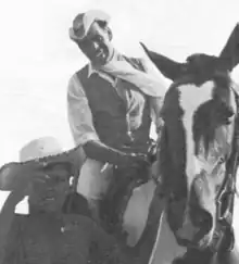 A black and white photograph of an Aboriginal male dressed as a cowboy on horseback next to an Aboriginal boy on foot