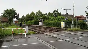 Side platform next to double-track railway line just beyond a level crossing