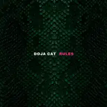 A photo of a nonspecific reptile's green scales, vertically symmetrical. The singer's name "Doja Cat" is shown in white at the center of the image. Beside it is the song title "Rules", shown in pink.