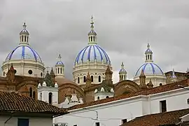 Roofs and towers of a small white church and a larger brown brick church with three large white-blue cuppolas.