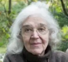 photograph of a headshot of an older woman with glasses and greenery in the background