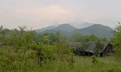 A green landscape with mountains in the back and a house towards the right.