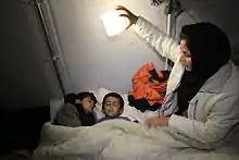 With no electricity in refugee camps in Idomeni Greece; Mother holds her solar lantern called the SolarPuff to check on her 2 little boys sleeping in sleeping bags.