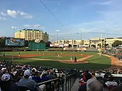 A baseball game on a green field as seen from the seating bowl behind home plate