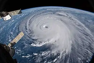 A photograph of a hurricane from space. The storm features a large eye and sprawling, curving cloud cover.