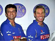 A dark coloured man in the left and a white coloured man in the right, both wearing blue shirts.