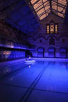 image shows a swimming pool at night with a small boat floating on it, 2 people are in the boat