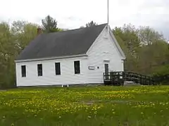 A view of Dry Mills one-room schoolhouse with a meadow filled with spring flowers.