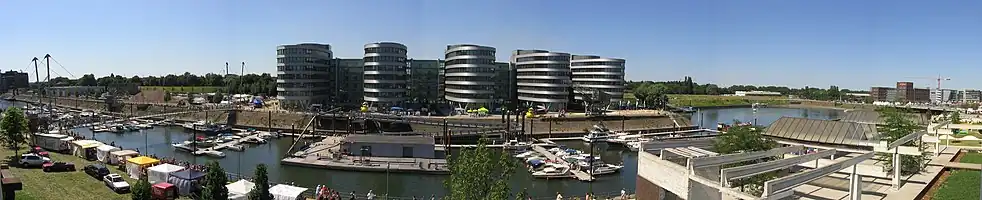 View of the Marina (left hand) and the "Five Boats" office complex, designed by the British architect Nicholas Grimshaw. On the right hand you can see the Holzhafen, which will be encircled by a projected hotel complex called Eurogate. The free space shown in the photograph to the left of Grimshaw's 'boat building' does not actually exist any more (used for the "Hitachi Power Office").