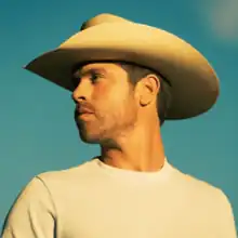 A photograph of Lynch looking to the side wearing a cowboy hat against a blue sky background