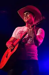 A young man wearing a white t-shirt and a cowboy hat, playing a guitar