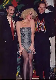 Three men standing together, two in suits and the middle one in drag